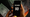 A hand holds a phone showing $0 on the screen, overlaid on an image of burning money.